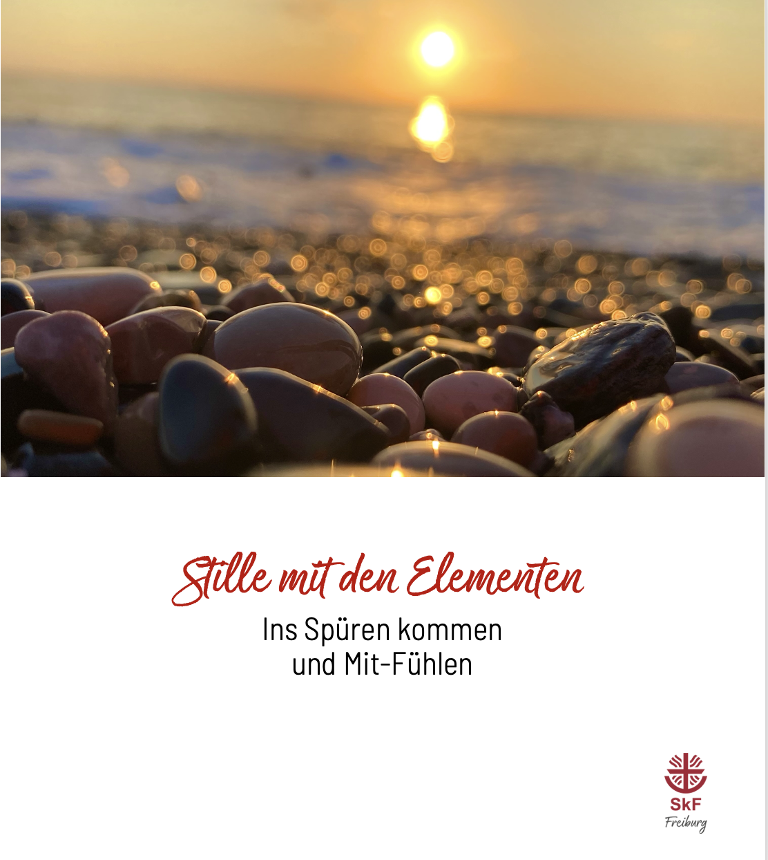 Nahaufnahme von bunten Kieselsteinen an einem Strand mit sanftem Sonnenlicht und Meereswellen im Hintergrund. Der Text darunter lautet: "Stille mit den Elementen. Ins Spüren kommen und Mit-Fühlen. SKF Freiburg.".