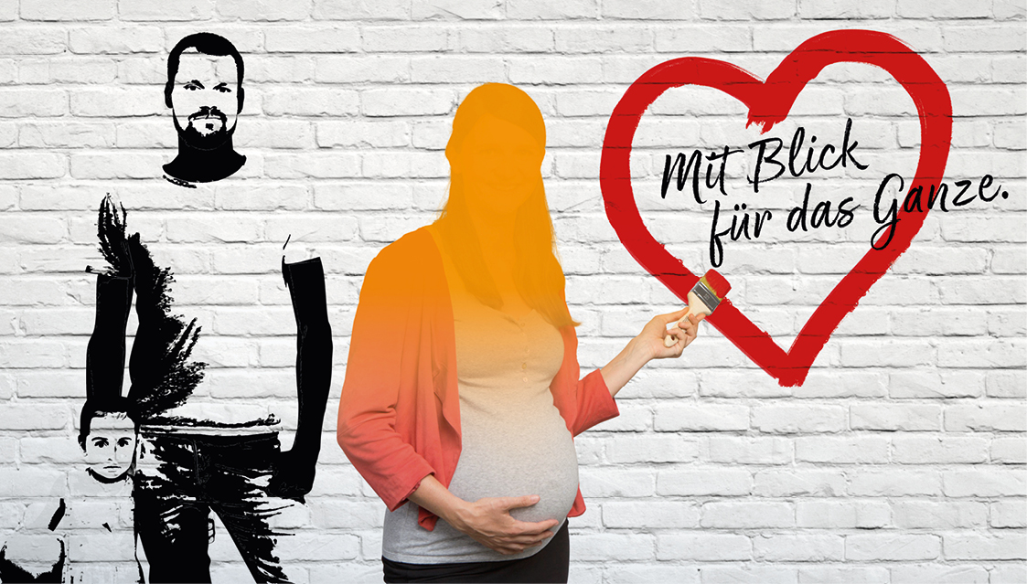 Eine schwangere Frau steht vor einer weißen Backsteinmauer und hält einen Pinsel in der Hand. Neben ihr ist ein gemaltes Herz mit deutschem Text zu sehen, und links davon sind ein Mann und ein Kind auf die Wand gemalt.