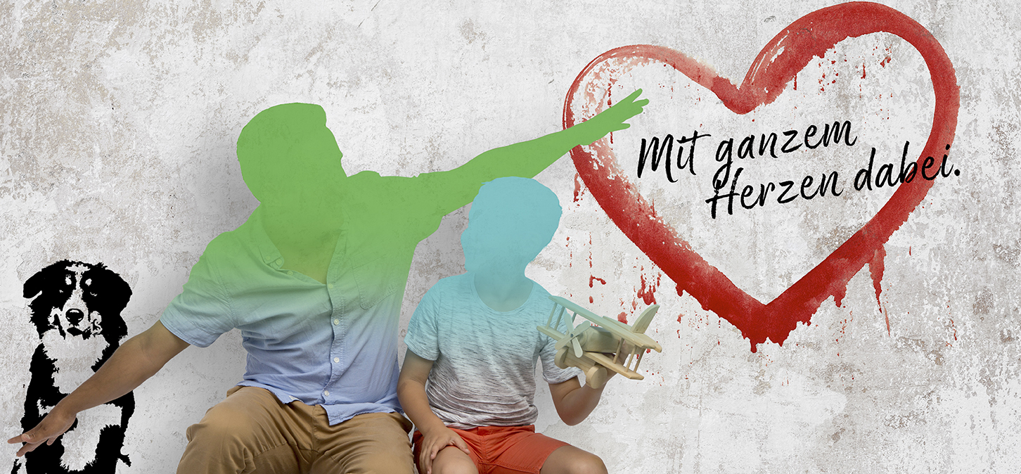 Ein Mann und ein Kind sitzen zusammen; der Mann gestikuliert in Richtung eines großen gemalten Herzens an einer Wand mit den deutschen Worten "Mit ganzem Herzen dabei". Eine schwarz-weiße Hundeillustration sitzt neben den beiden. Das Kind hält ein hölzernes Spielzeugflugzeug in der Hand.