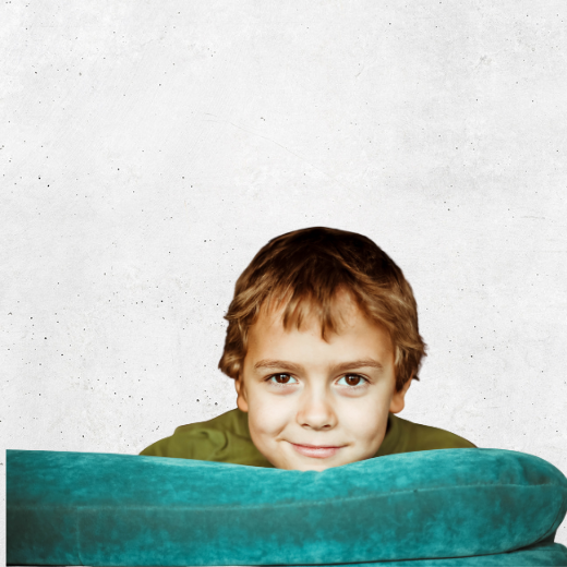 Ein lächelnder kleiner Junge mit kurzen braunen Haaren schaut vor dem Hintergrund einer weiß strukturierten Wand über die Rückenlehne eines blaugrünen Sofas hinweg. Ein lächelnder kleiner Junge mit kurzen braunen Haaren schaut vor dem Hintergrund einer weiß strukturierten Wand über die Rückenlehne eines blaugrünen Sofas hinweg.